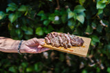 Sliced cooked steak with salt flakes on a wooden board, held outdoors