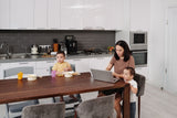 Busy mom working on her laptop while her kids eat breakfast in the kitchen