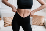 Woman in a black workout top and high-waisted leggings adjusting her waistband